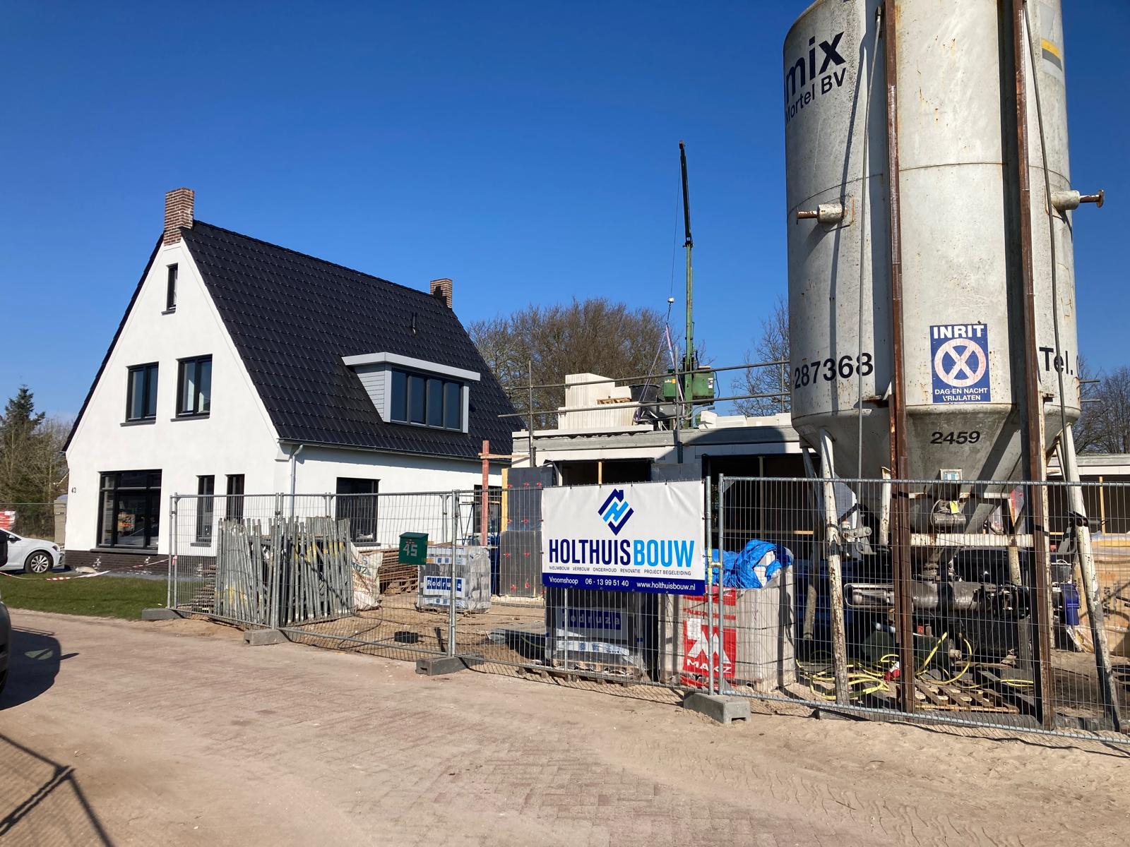 Woning in aanbouw met steigers en een dak afgedekt met blauwe folie en panlatten